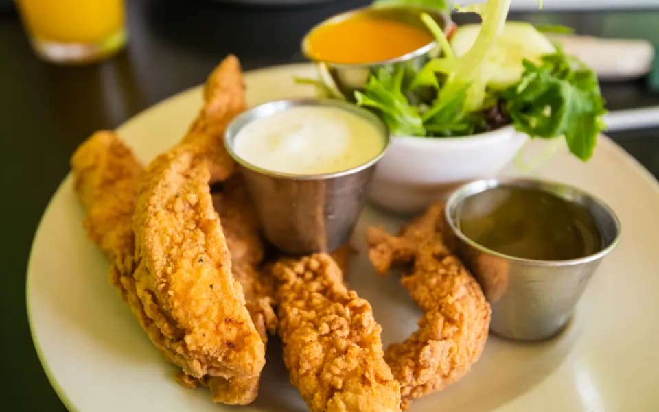 Tiras de Pollo Crispy: Tiras de pechuga apanadas y bien crocantes, con papas a la francesa y salsa miel