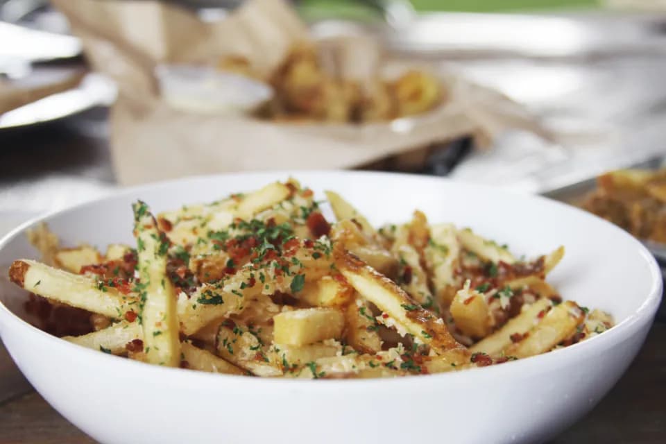 Papas Pocho Cargadas: Papas crocantes bañadas en queso cheddar fundido, tocineta picada, cebollín y un